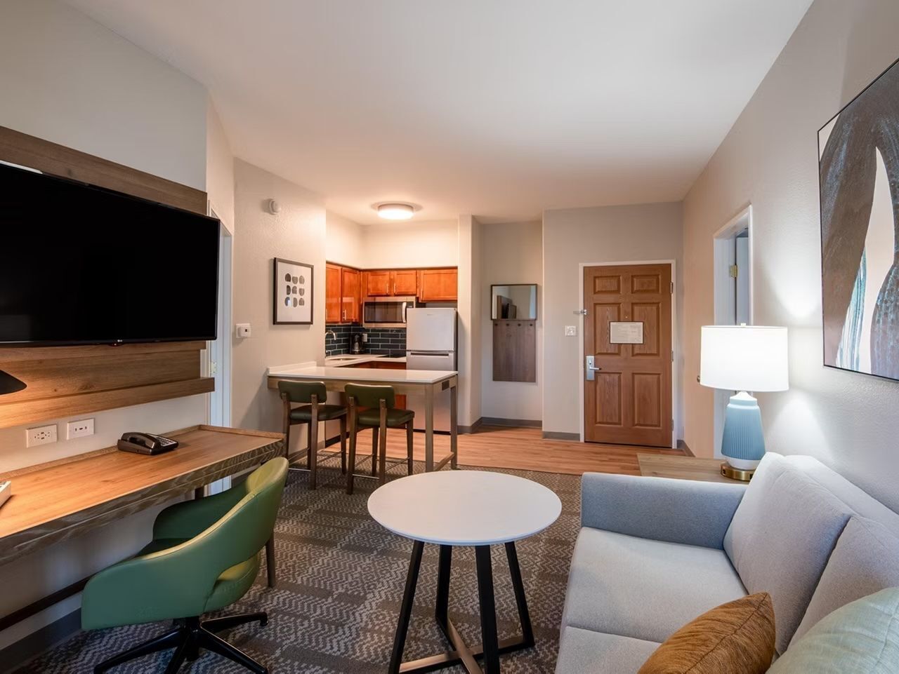Ein kompaktes Hotelzimmer mit Küchenzeile, Essecke, einer Couch und einem Flachbildfernseher.