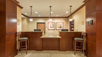 A reception area with wooden paneling, two bar stools, a reception desk, framed artwork, and a door labeled "CAN".