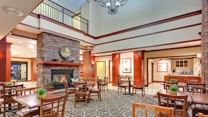 A spacious lobby with a stone fireplace, multiple dining tables and chairs, and a second-floor balcony. - Accessible 1BR 2 Queen Suite | Pool + Breakfast! (Glendale)