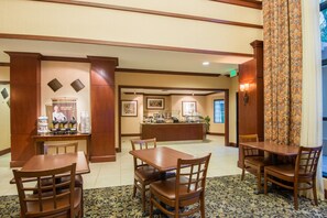 A hotel lobby with a reception desk, a buffet area, and several wooden tables and chairs.