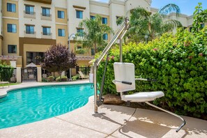 A swimming pool with a sun lounger and a metal chair, surrounded by greenery and a building with balconies. - Accessible 1BR 2 Queen Suite | Pool + Breakfast! (Glendale)