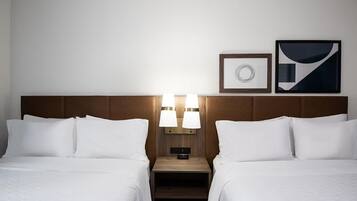 A hotel room with two beds, a nightstand with lamps, a clock, and two framed pictures on the wall.