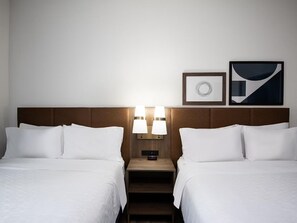 A hotel room with two beds, a nightstand with lamps, a clock, and two framed pictures on the wall.