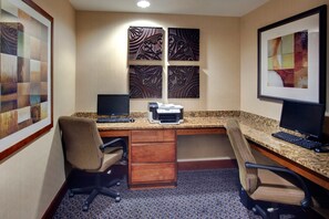 A hotel office with a desk, two chairs, a printer, and framed artwork on the walls.