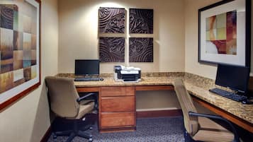 A hotel office with a desk, two chairs, a printer, and framed artwork on the walls.