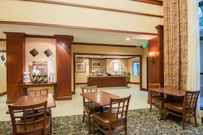 A hotel lobby with a reception desk, a buffet area, and several wooden tables and chairs.