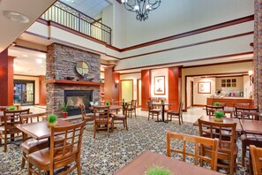 A spacious lobby with a stone fireplace, multiple dining tables and chairs, and a second-floor balcony.