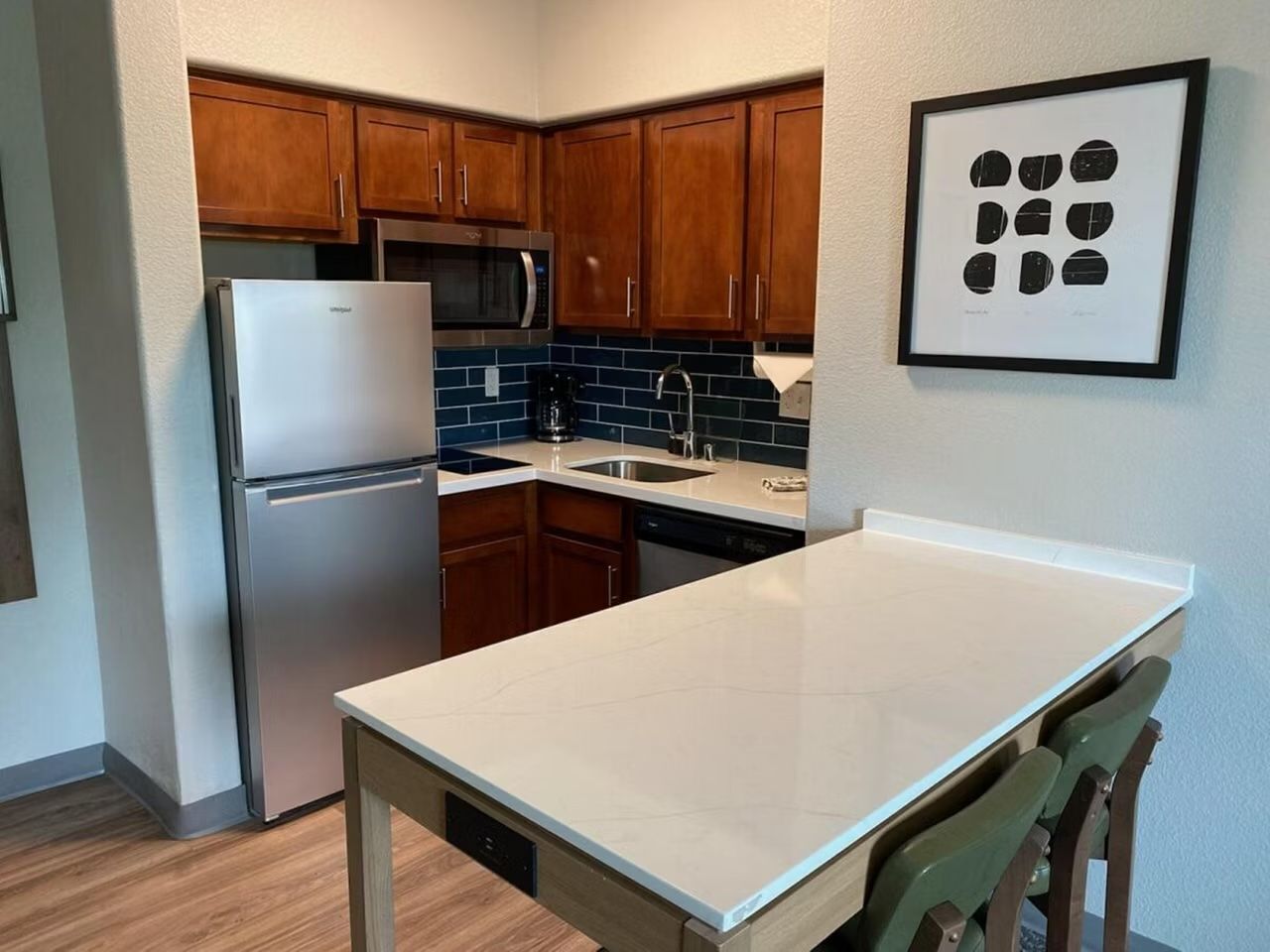 A compact kitchen with wooden cabinets, a stainless steel refrigerator, a microwave, and a sink.
