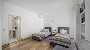 Ein Schlafzimmer mit zwei Betten, einem Nachttisch mit Lampe, einer kleinen Zimmerpflanze und einem Bücherregal.