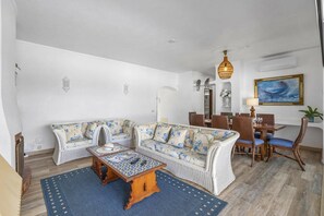 A living room with a sofa, a coffee table, wicker chairs, a dining table, and a painting on the wall. - Villa Felicidade by Villa Plus (Olhos de Água)