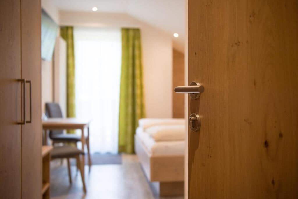 A hotel room with a wooden door, a bed, a desk, and a chair.