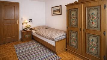Un dormitorio con un armario de madera, una cama con ropa de cama a cuadros, una mesita de noche con lámpara, y un cuadro en la pared.