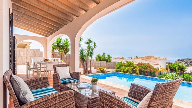Eine Terrasse im Freien mit Korbmöbeln, einem Pool und Blick auf das Meer.