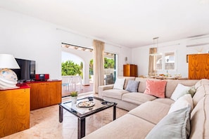 A modern living room with a sofa, coffee table, TV, and a view of the outdoors. - Villa La Serena by Villa Plus (Cala en Porter)