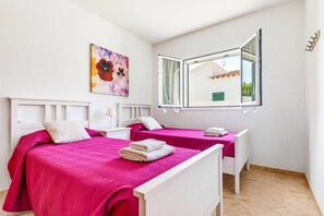 A bedroom with two beds, a window with a view, and a painting on the wall. - Villa La Serena by Villa Plus (Cala en Porter)