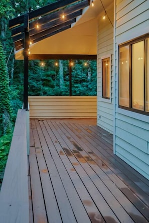 Eine Holzterrasse mit Lichterketten, einem überdachten Bereich und einem Gebäude mit großen Fenstern.