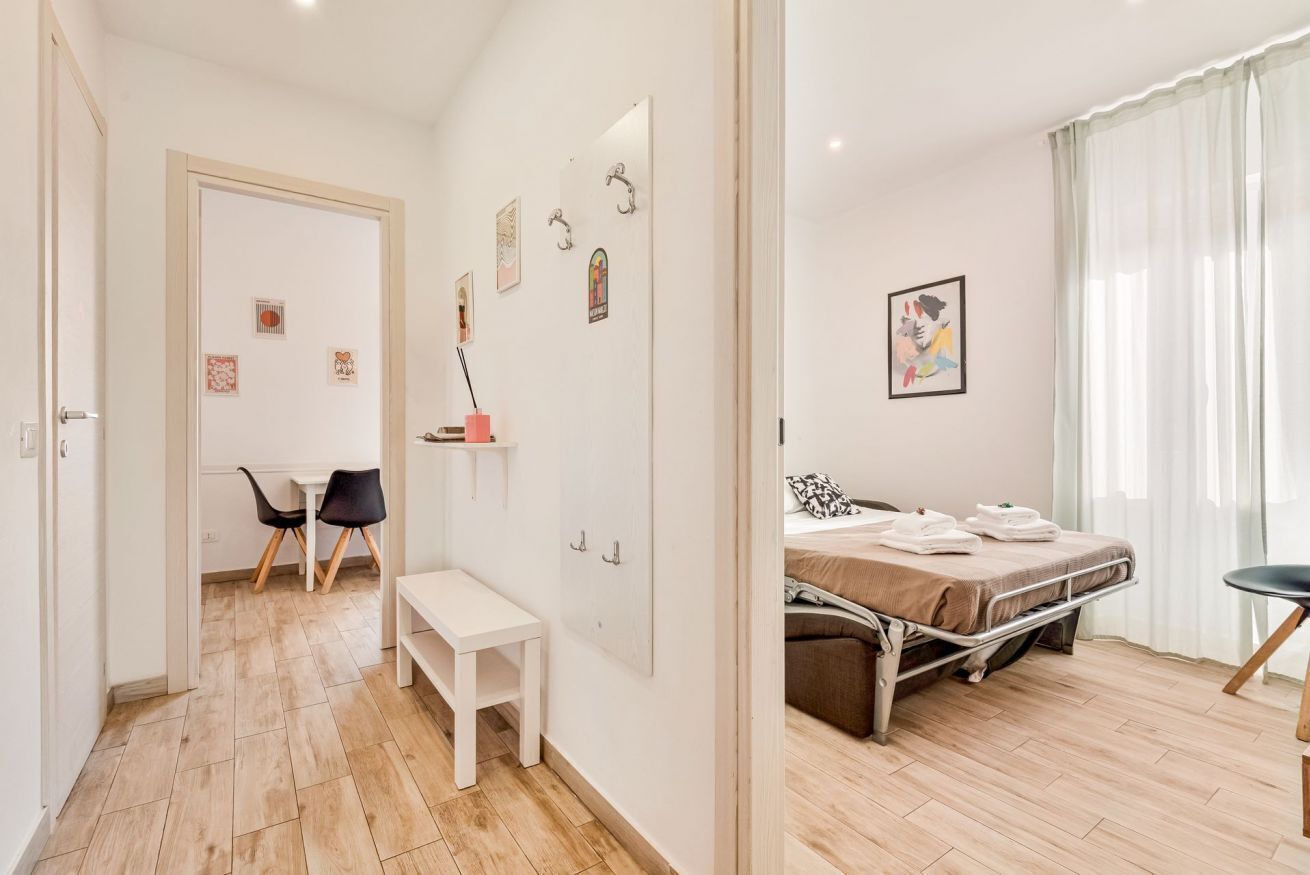 Une chambre à coucher avec un lit, une table de chevet et une chaise. Une petite table et des chaises se trouvent dans la pièce adjacente.