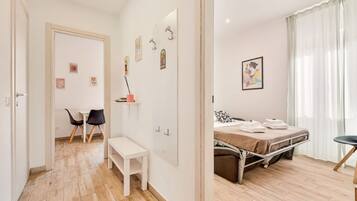 Un dormitorio con cama, mesita de noche y una silla. En la habitación contigua, hay una pequeña mesa y sillas.