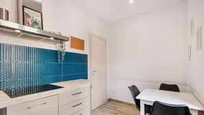 Una cocina moderna con salpicadero de azulejos azules, una campana extractora de acero inoxidable y una mesa de comedor blanca con sillas negras.