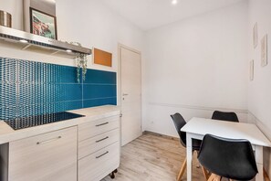 Et moderne køkken med blå flisebordsplade, emhætte i rustfrit stål og et hvidt spisebord med sorte stole.
