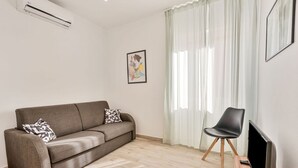 Una sala de estar con sofá, sillón, televisor de pantalla plana y ventana con cortinas.