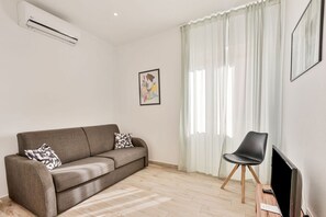A living room with a sofa, a chair, a flat-screen TV, and a window with curtains.