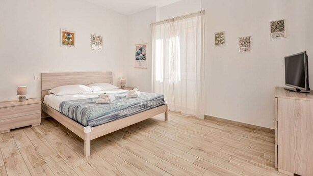 Un dormitorio con una cama de madera, mesitas de noche, un televisor y obras de arte en las paredes.