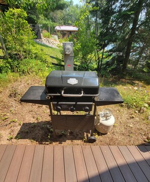 A portable grill on a wooden deck with a gas tank beside it.