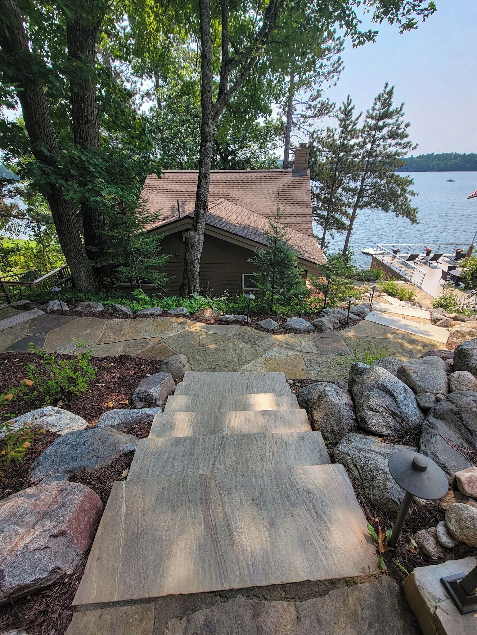 A stone pathway leading to a cabin by a lake, surrounded by rocks and trees.