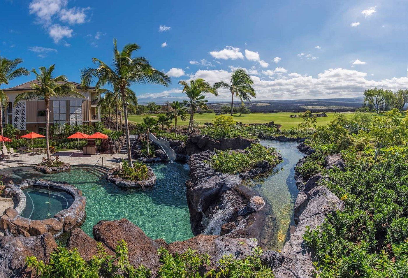 A resort with a pool, palm trees, and a view of the landscape.