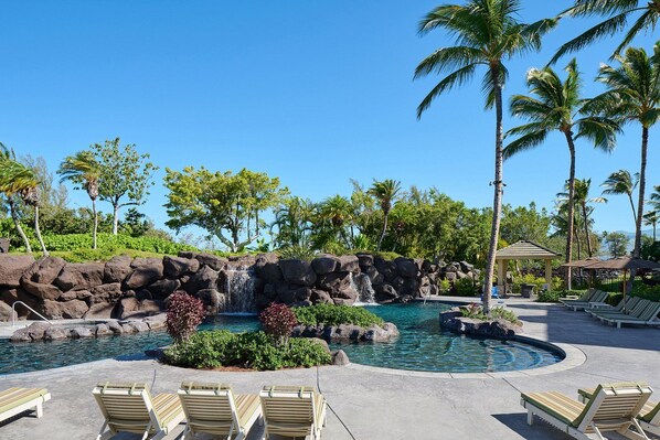 A resort pool area with multiple pools, lounge chairs, and palm trees.
