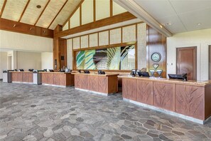 Un espace d’accueil doté d’un sol carrelé en pierre, de comptoirs de réception en bois et d’un grand tableau abstrait accroché au mur.