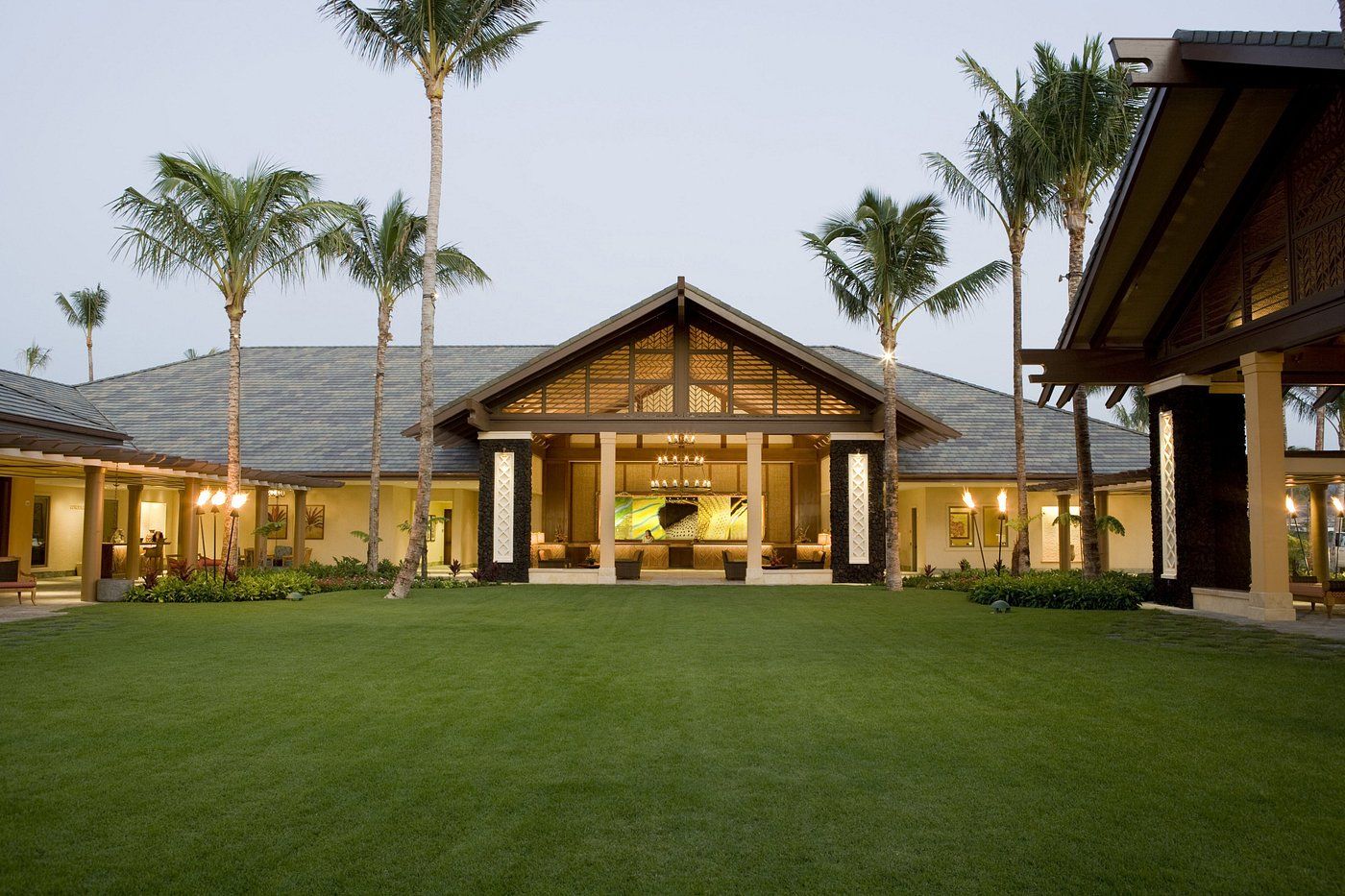 A modern resort with a covered outdoor area, palm trees, and a well-maintained lawn.