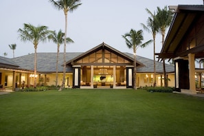 Un resort moderno con un espacio exterior cubierto, palmeras y un césped bien cuidado.