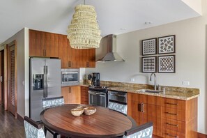 Une cuisine moderne avec des meubles en bois, des appareils électroménagers en acier inoxydable, une table de salle à manger ronde et des œuvres d’art décoratives au mur.