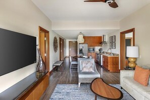 Un salon moderne avec un canapé, une table basse, un téléviseur et une cuisine en arrière-plan.
