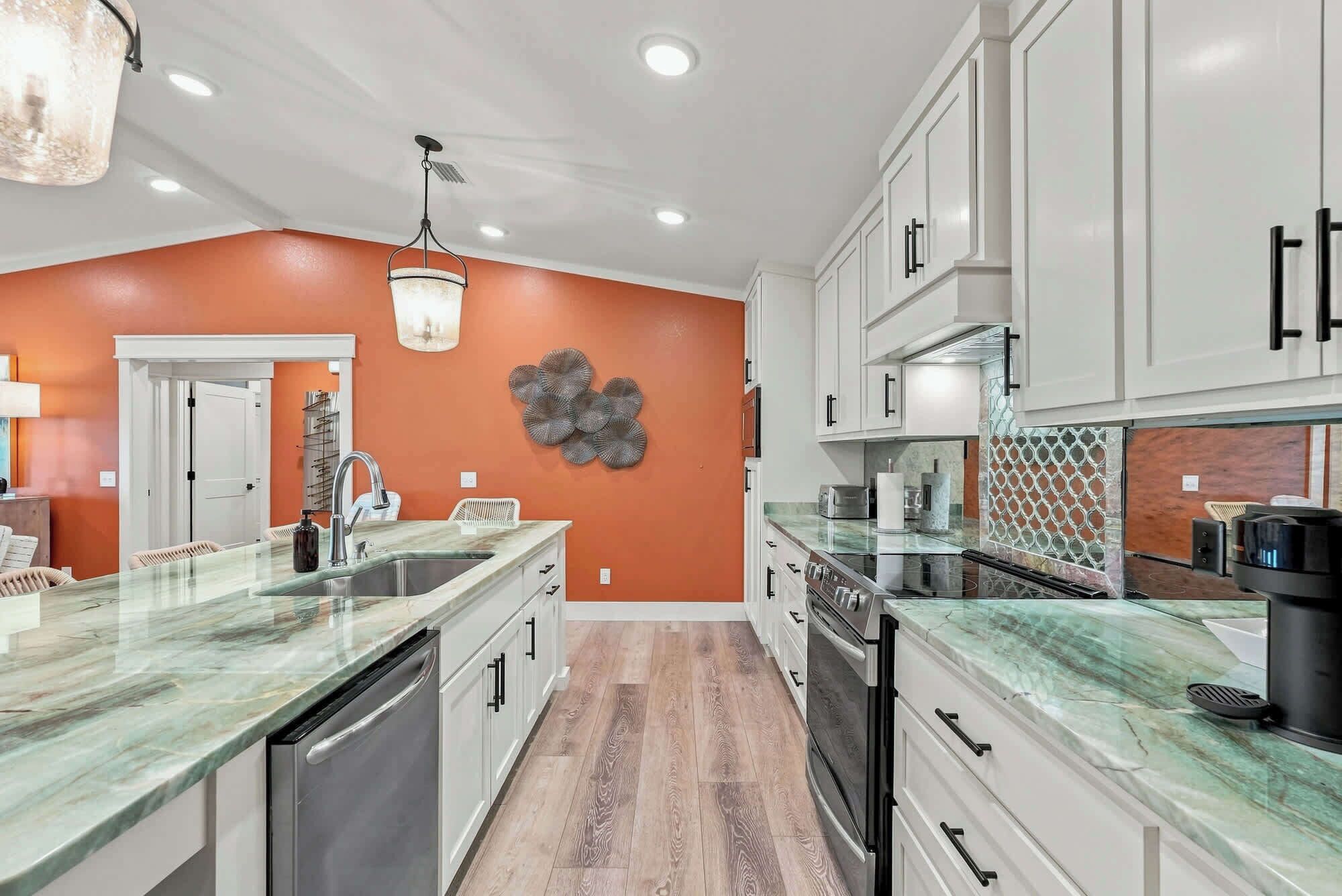 A modern kitchen with white cabinets, a marble countertop, and a wooden floor.