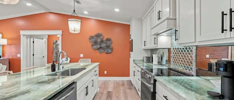 Una cocina moderna con armarios blancos, encimera de mármol y suelo de madera.