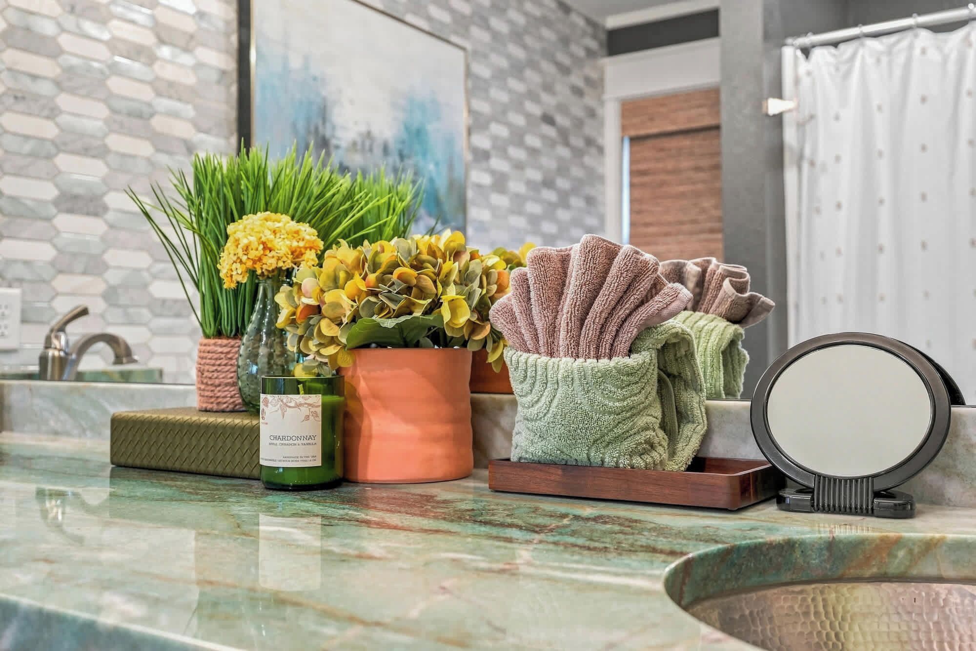 Un tocador de baño con espejo, una botella de Chardonnay y plantas decorativas.