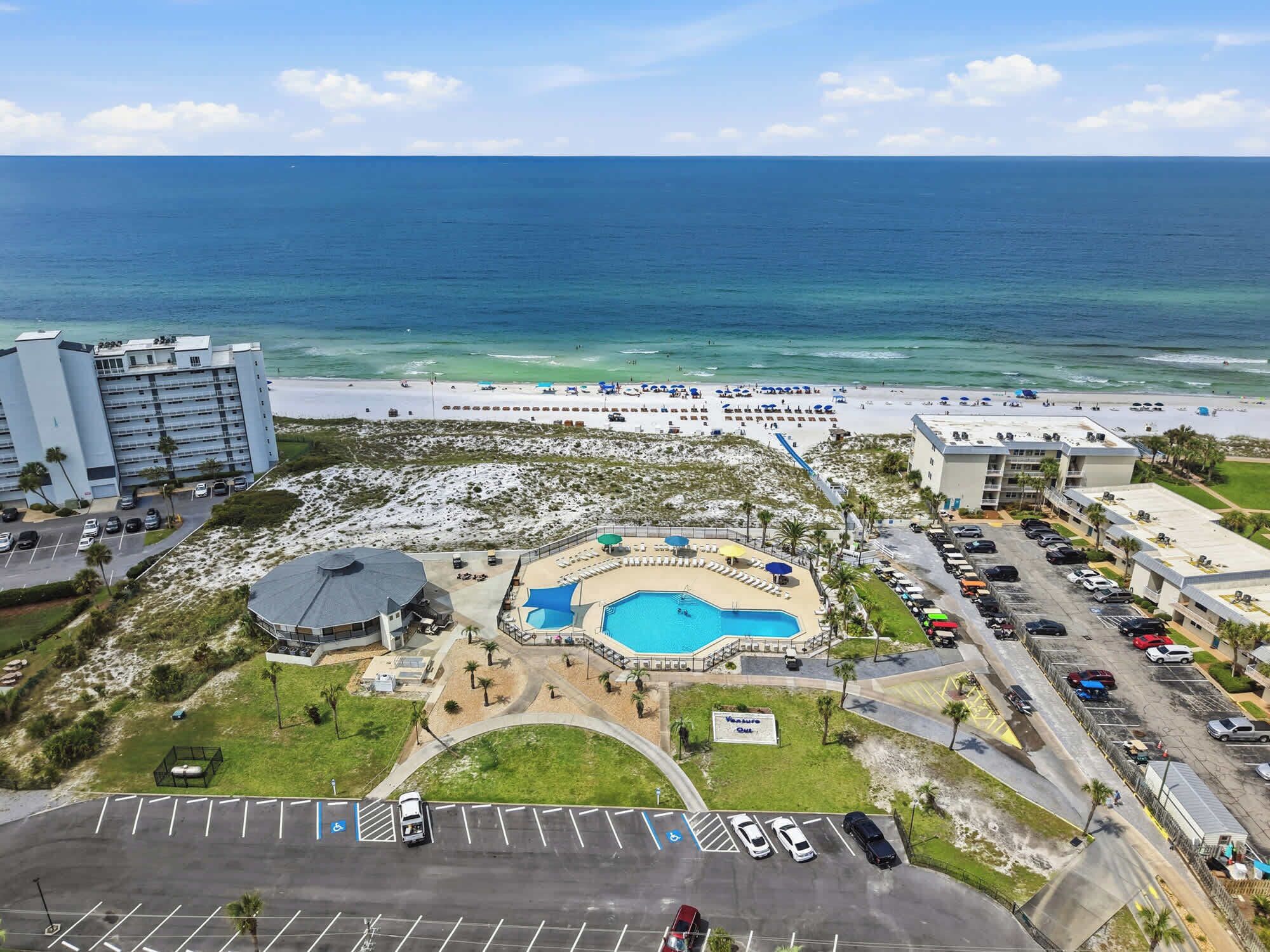 A resort with a swimming pool, beach access, and a parking lot.