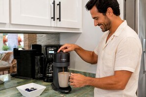 Eine Person bedient eine Kaffeemaschine in einer Küche mit weißen Schränken und einer Marmorarbeitsplatte.