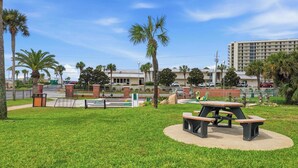 Un parque con una mesa de picnic y bancos, rodeado de palmeras y un edificio al fondo.