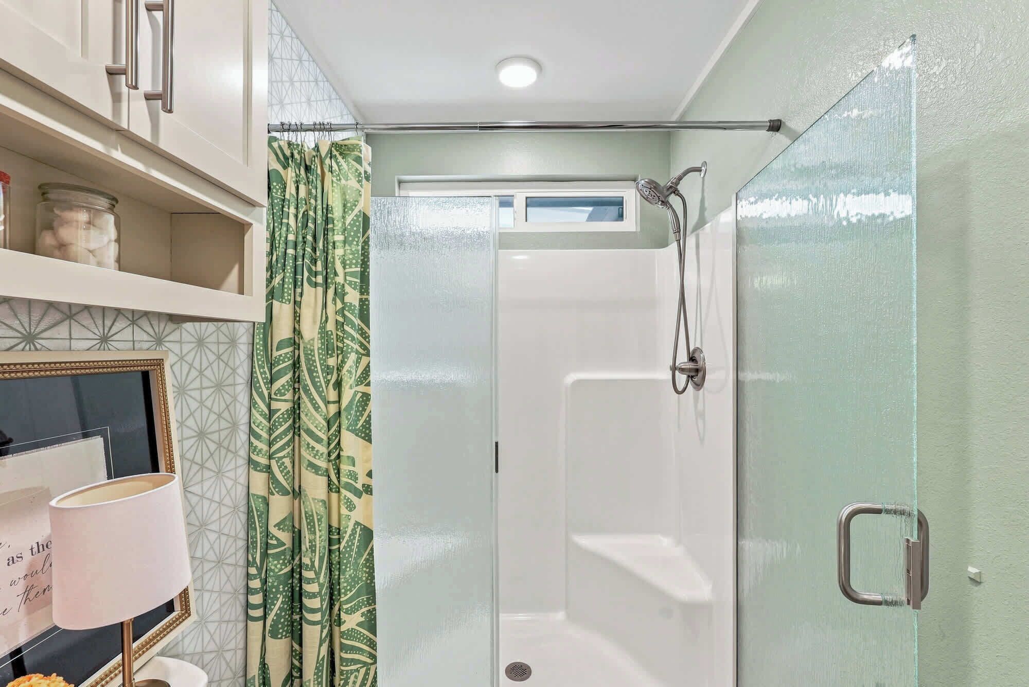 A bathroom with a shower, a glass door, and a shelf with toiletries.