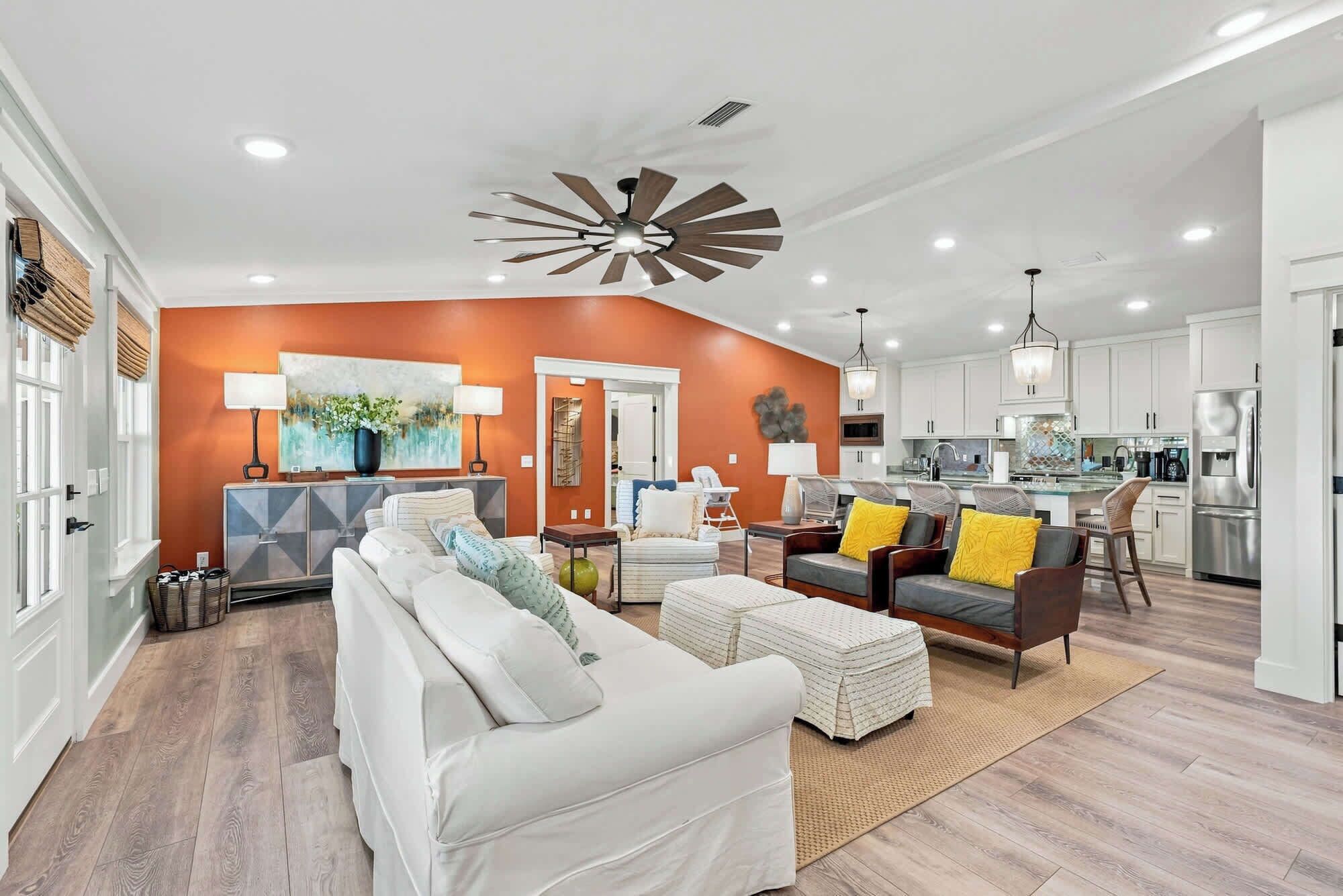 A modern living room with a white sofa, a dining area with a bar, and a kitchen with stainless steel appliances.