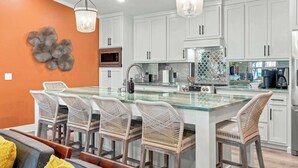 Una cocina moderna con armarios blancos, una isla de cristal y sillas de mimbre.