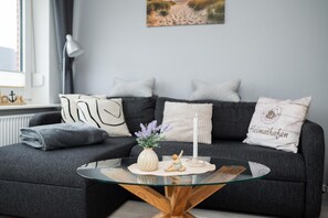 Ein modernes Wohnzimmer mit einem dunkelgrauen Sofa, einem Glastisch und dekorativen Kissen.