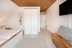 Ein Schlafzimmer mit einem Bett, einem Nachttisch, einem Schrank, einem Fernseher und einem Flur, der in einen anderen Raum führt.