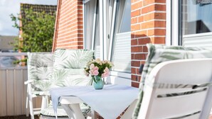 Eine Terrasse mit weißen Stühlen und einem Tisch, eine Vase mit Blumen sowie eine Ziegelwand im Hintergrund.
