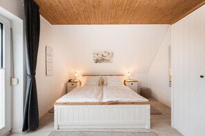 A bedroom with a wooden ceiling, a bed with a white headboard, two bedside tables with lamps, and a wall-mounted picture. - Apartment 'Katja' with Private Terrace and Wi-Fi (Büsum)