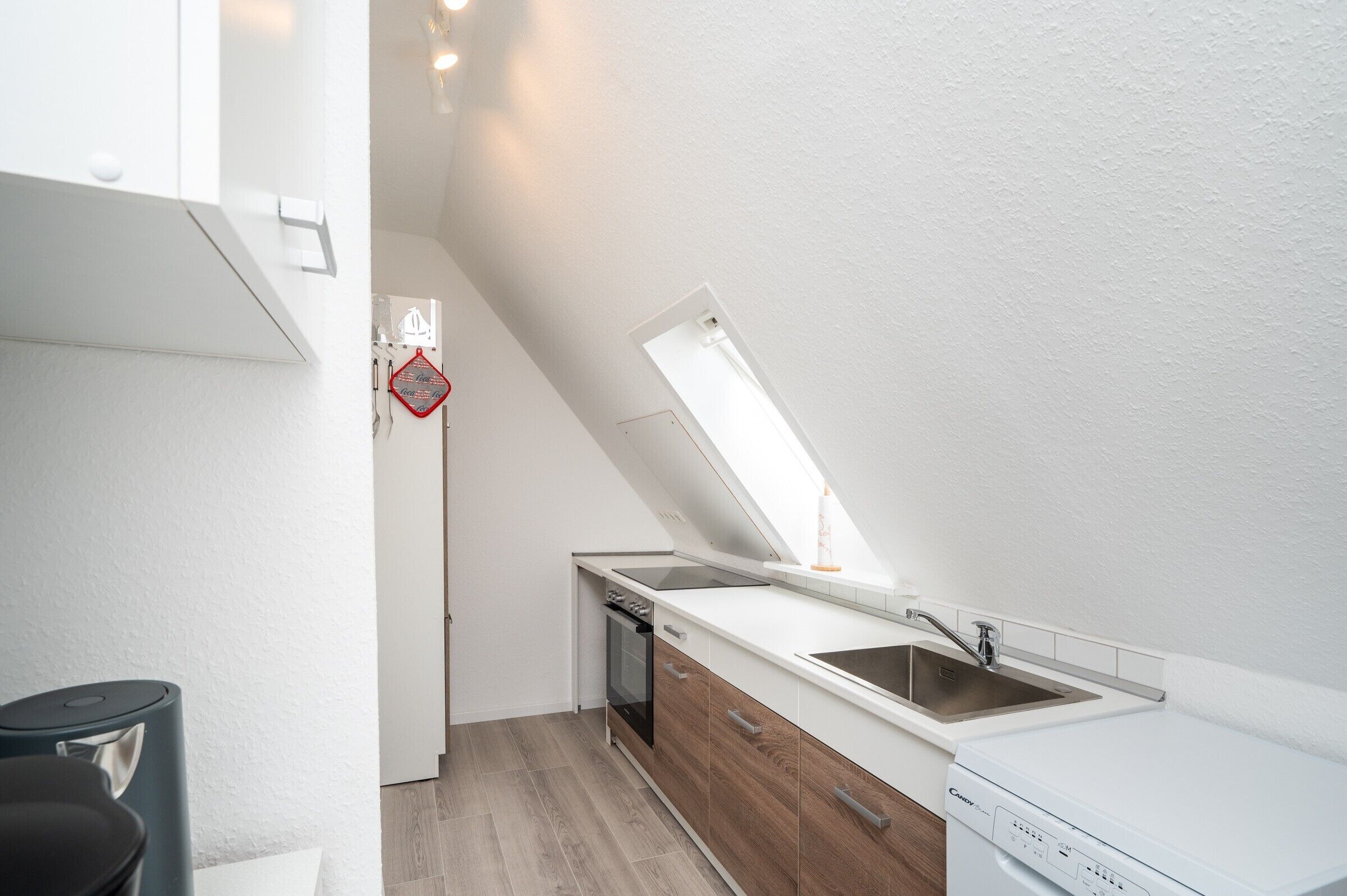 Eine kleine Küche mit integriertem Geschirrspüler, Spüle und Fenster für natürliches Licht.